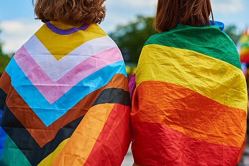 two women with LGBT flags draped over their shoulders